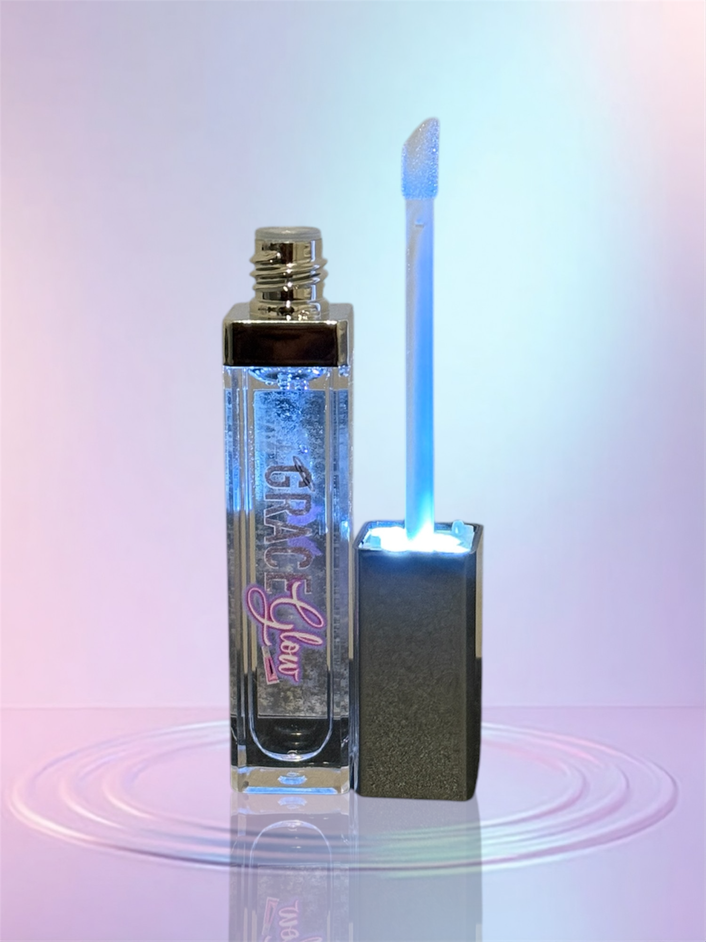 Clear lip gloss tube standing next to an open applicator wand illuminated by a soft blue LED light, showcasing the LED light up tube with attached mirror.