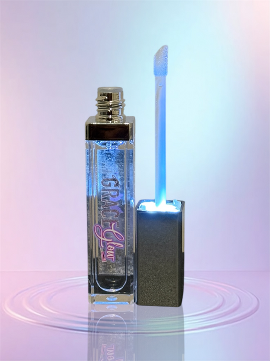 Clear lip gloss tube standing next to an open applicator wand illuminated by a soft blue LED light, showcasing the LED light up tube with attached mirror.